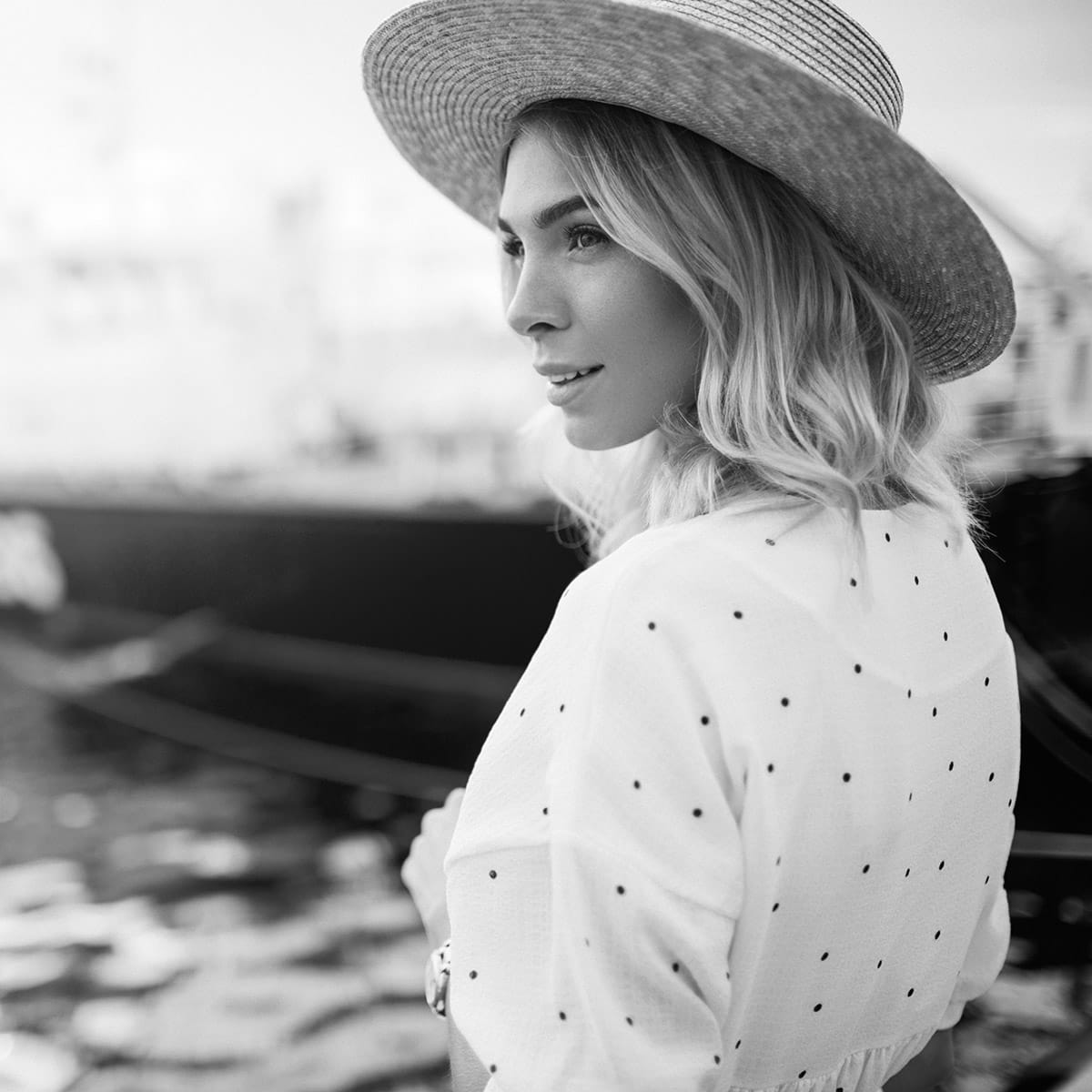tummy tuck patient model in a sun hat and polka dot dress looking over a body of water