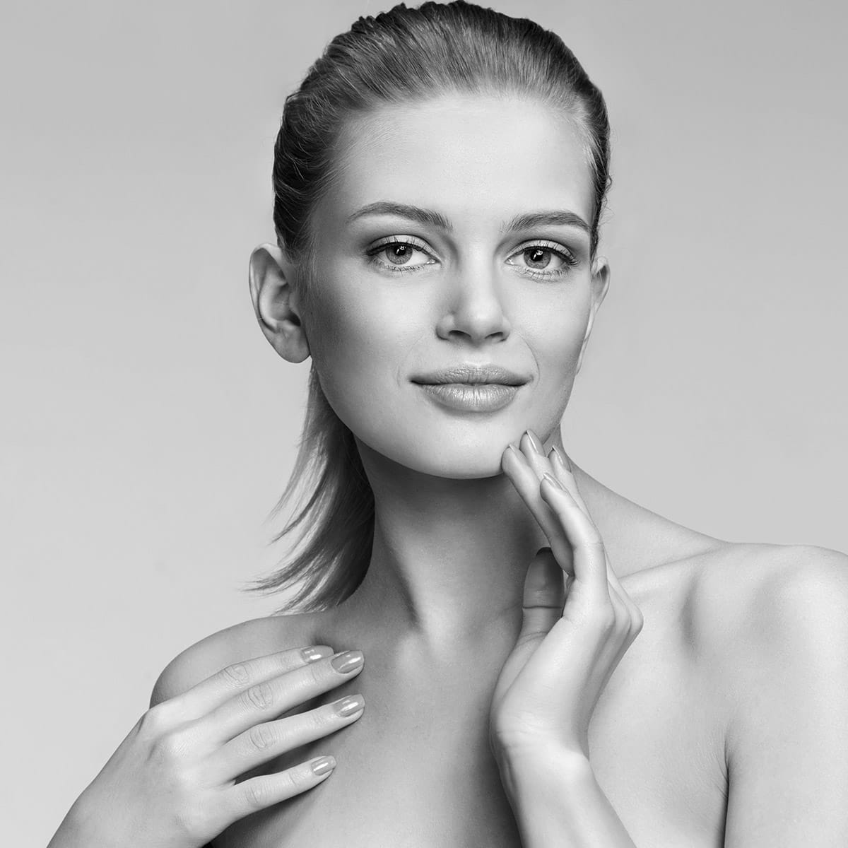 botox patient model softly smiling with bare shoulders while touching her face